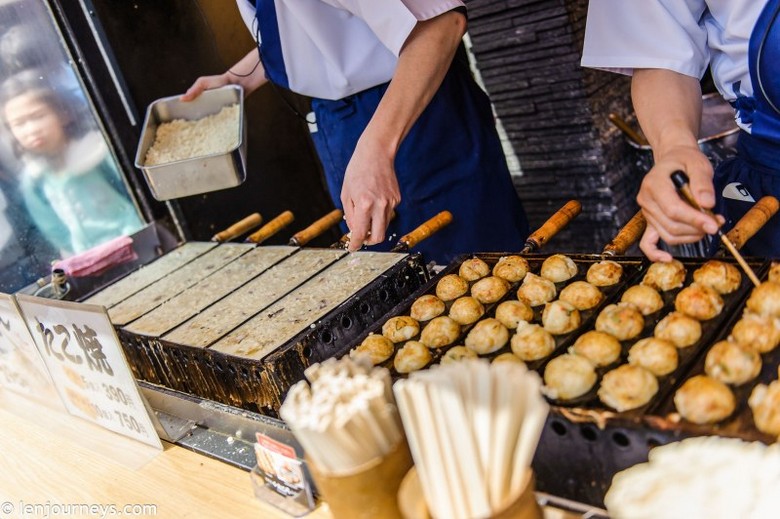 Người bán đang xoay từng viên takoyaki bằng que trên khuôn gang nóng